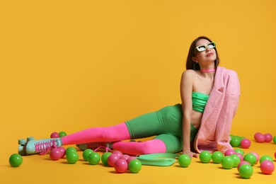 Photo of Stylish woman with retro roller skates and colorful balls on orange background. Space for text