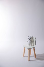 Photo of Cute crocheted bear on wooden chair against white background, space for text