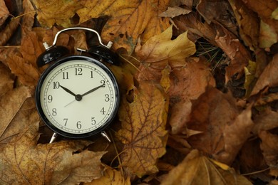 Photo of Autumn time. Alarm clock on fallen leaves, top view with space for text