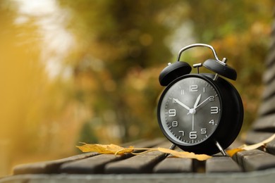 Photo of Autumn time. Alarm clock on bench in park, closeup. Space for text