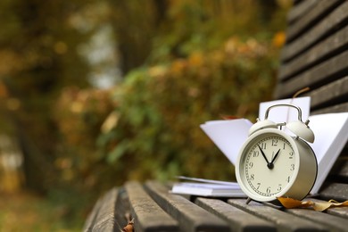 Photo of Autumn time. Alarm clock and book on bench in park, closeup. Space for text