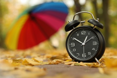 Photo of Autumn time. Alarm clock and umbrella in park, selective focus. Space for text