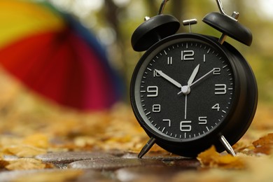 Photo of Autumn time. Alarm clock and umbrella in park, selective focus. Space for text