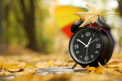 Photo of Autumn time. Alarm clock and umbrella in park, selective focus. Space for text