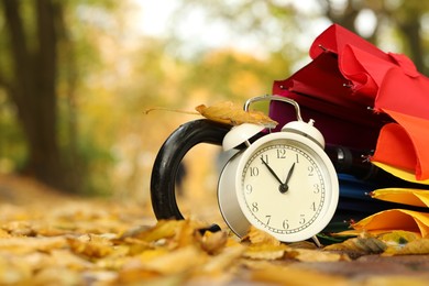 Photo of Autumn time. Alarm clock and umbrella in park, closeup