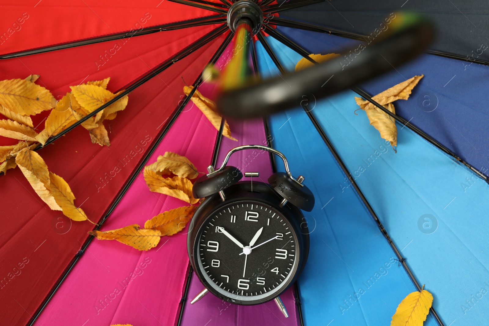 Photo of Autumn time. Alarm clock and fallen leaves on colorful umbrella