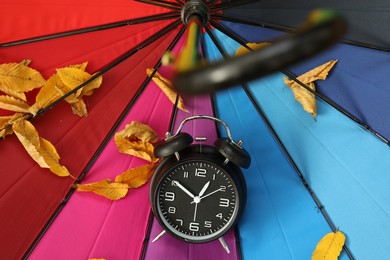 Photo of Autumn time. Alarm clock and fallen leaves on colorful umbrella