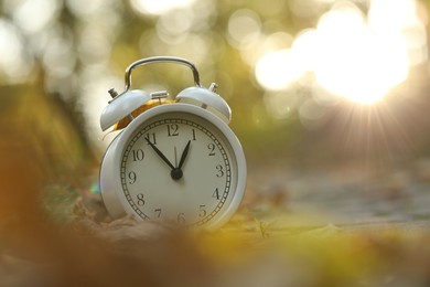 Photo of Autumn time. Alarm clock and fallen leaves on pathway in park, closeup with space for text