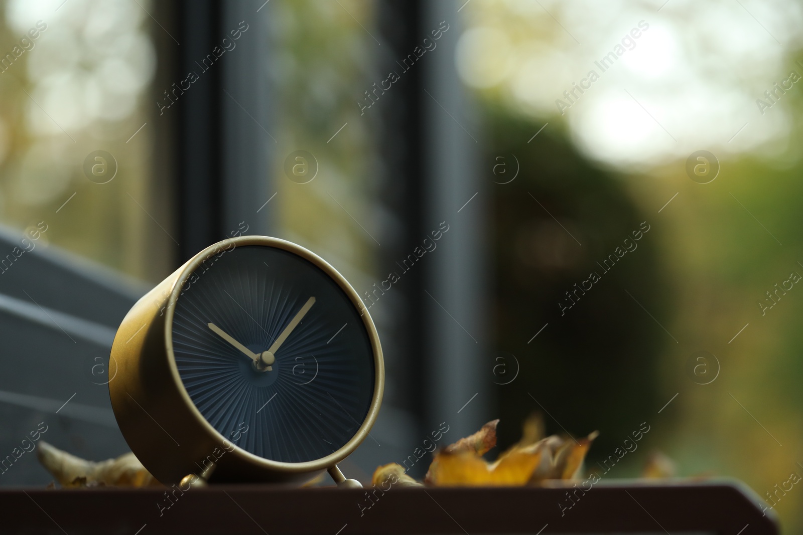 Photo of Autumn time. Alarm clock and fallen leaves near cafe outdoors, space for text