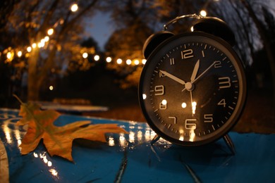 Photo of Autumn time. Alarm clock and fallen leaves on blue surface in evening park, wide angle lens