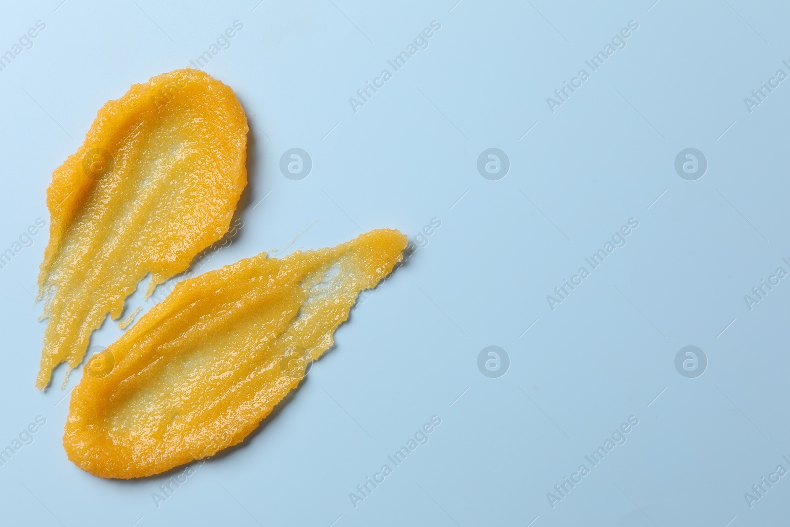 Photo of Smears of body scrub on light blue background, top view. Space for text