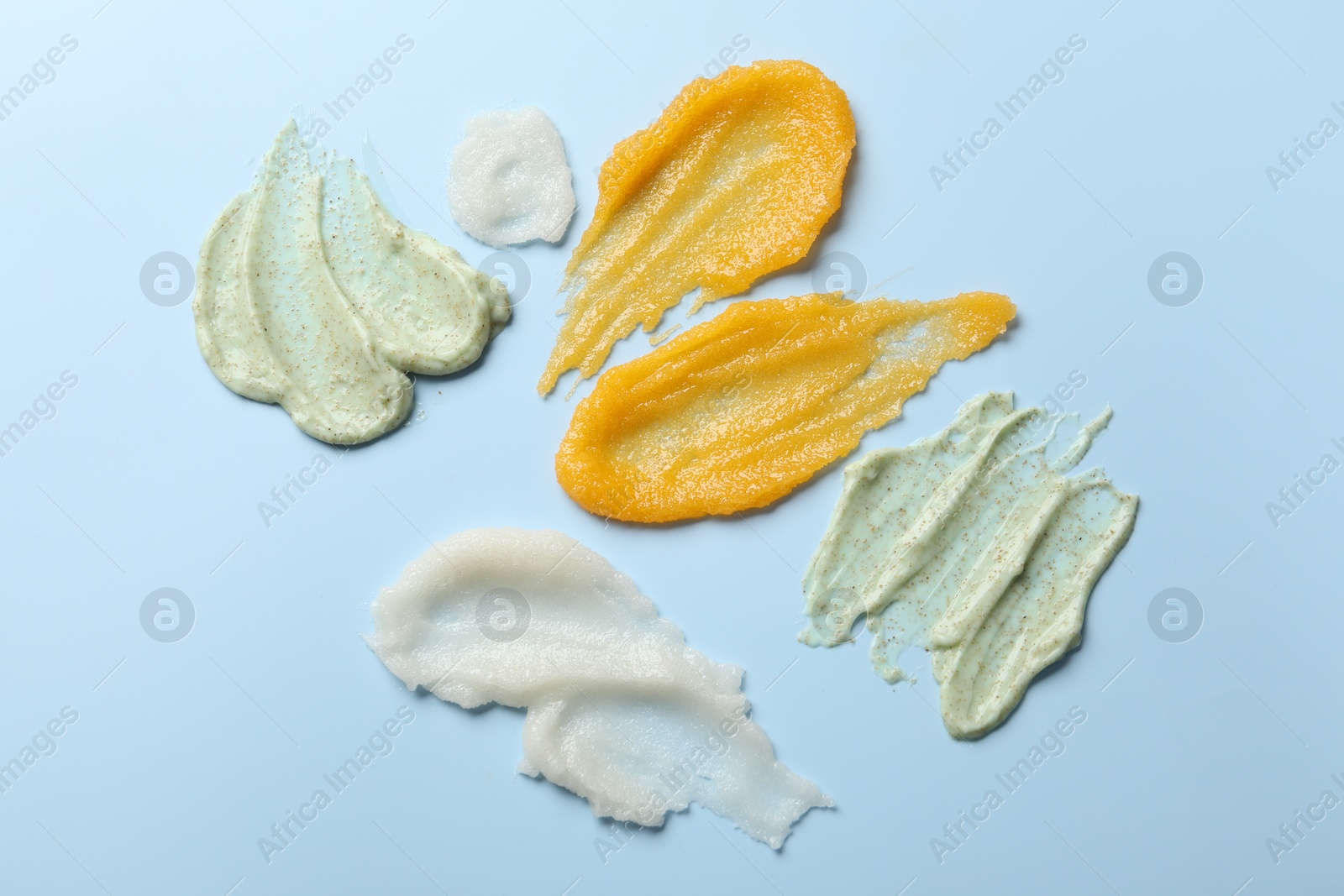 Photo of Smears of different body scrubs on light blue background, flat lay