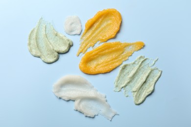 Photo of Smears of different body scrubs on light blue background, flat lay