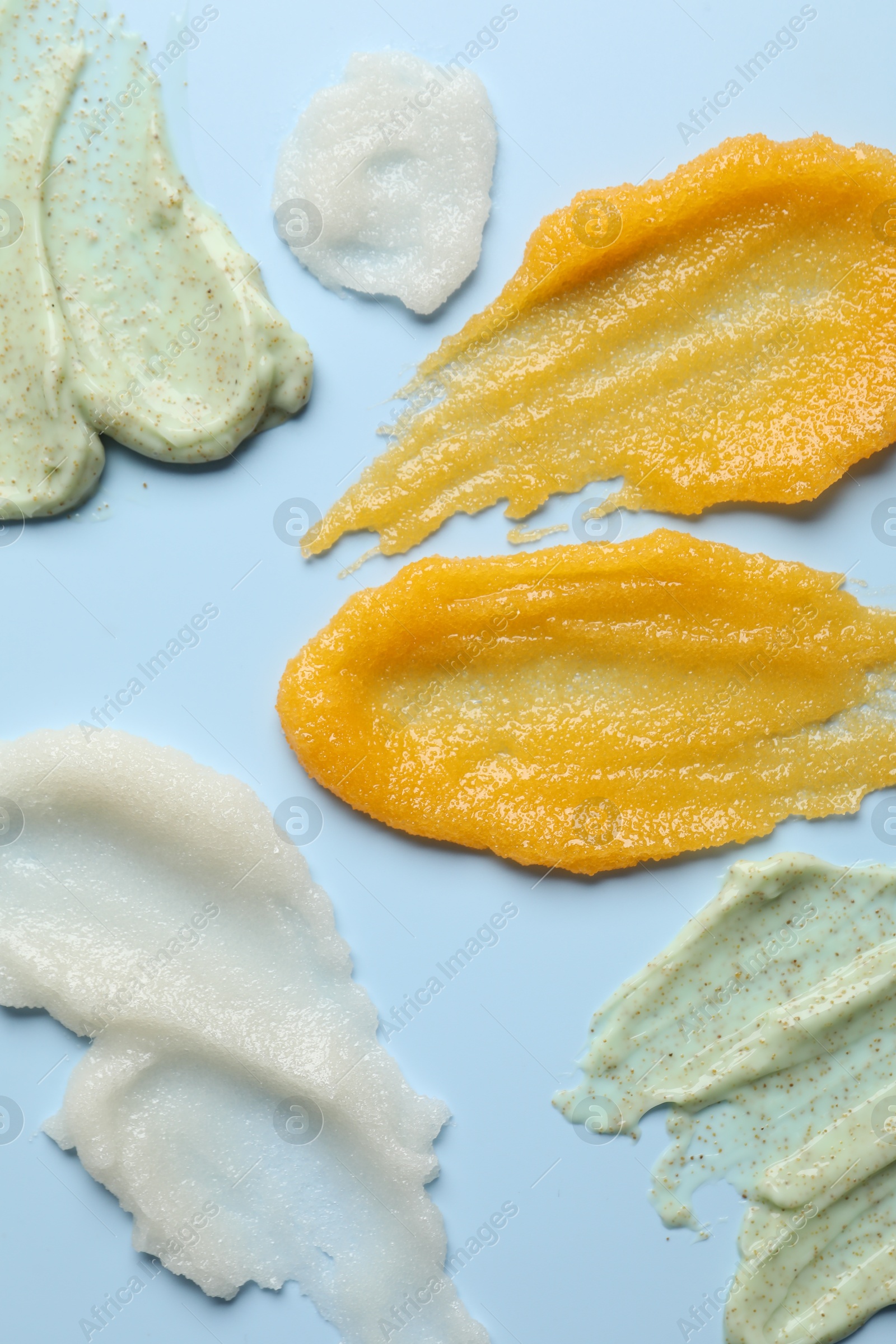 Photo of Smears of different body scrubs on light blue background, flat lay