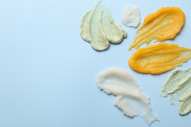 Photo of Smears of different body scrubs on light blue background, flat lay. Space for text