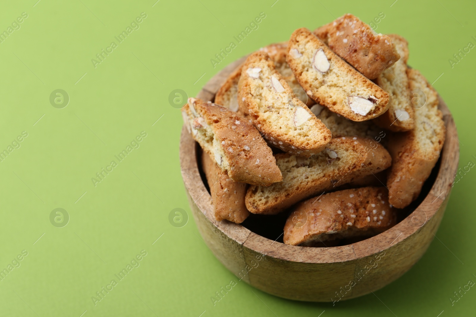 Photo of Traditional Italian almond biscuits (Cantucci) in bowl on green background, closeup. Space for text