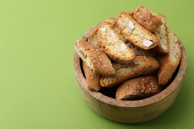 Photo of Traditional Italian almond biscuits (Cantucci) in bowl on green background, closeup. Space for text