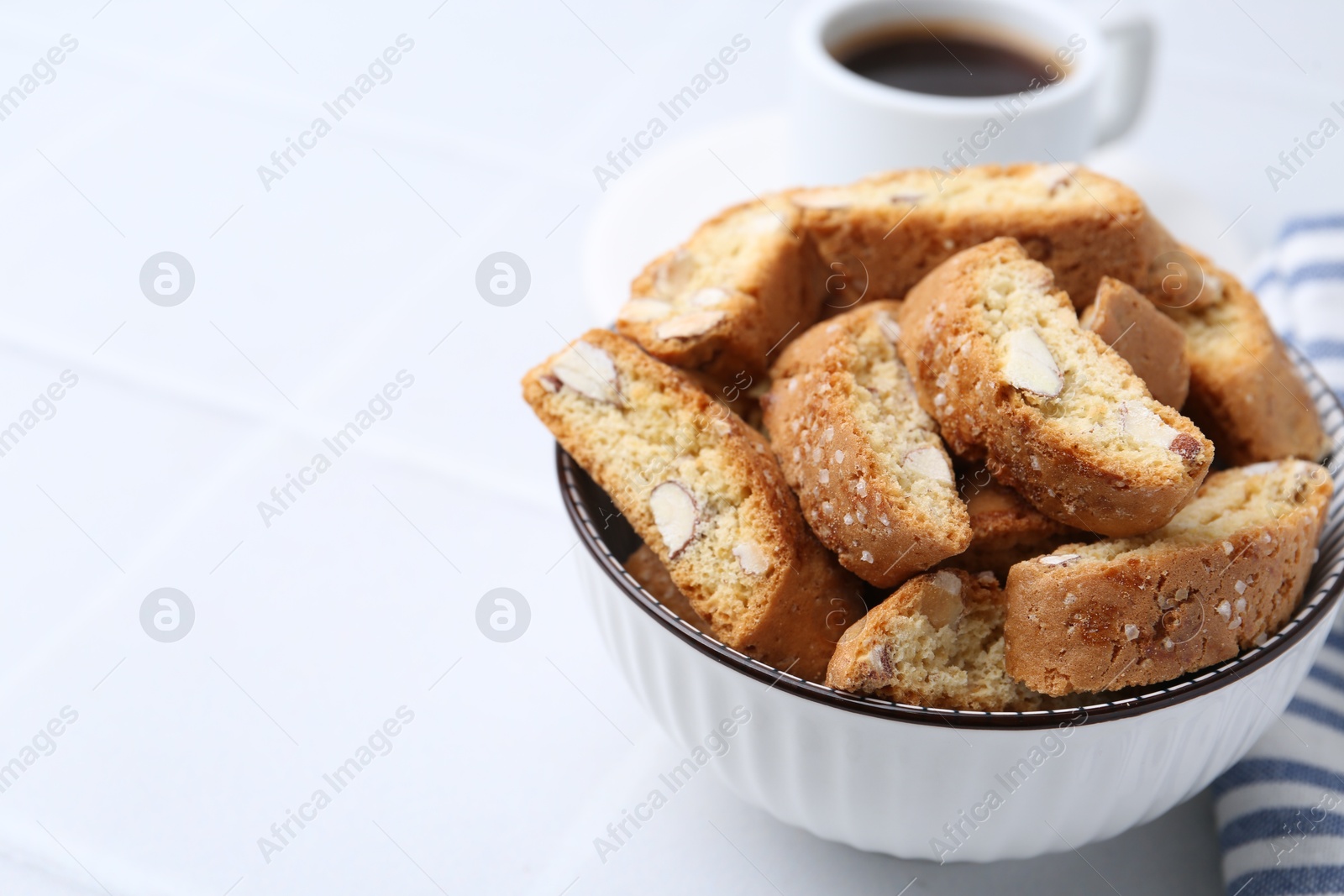 Photo of Traditional Italian almond biscuits (Cantucci) in bowl on white table, closeup. Space for text