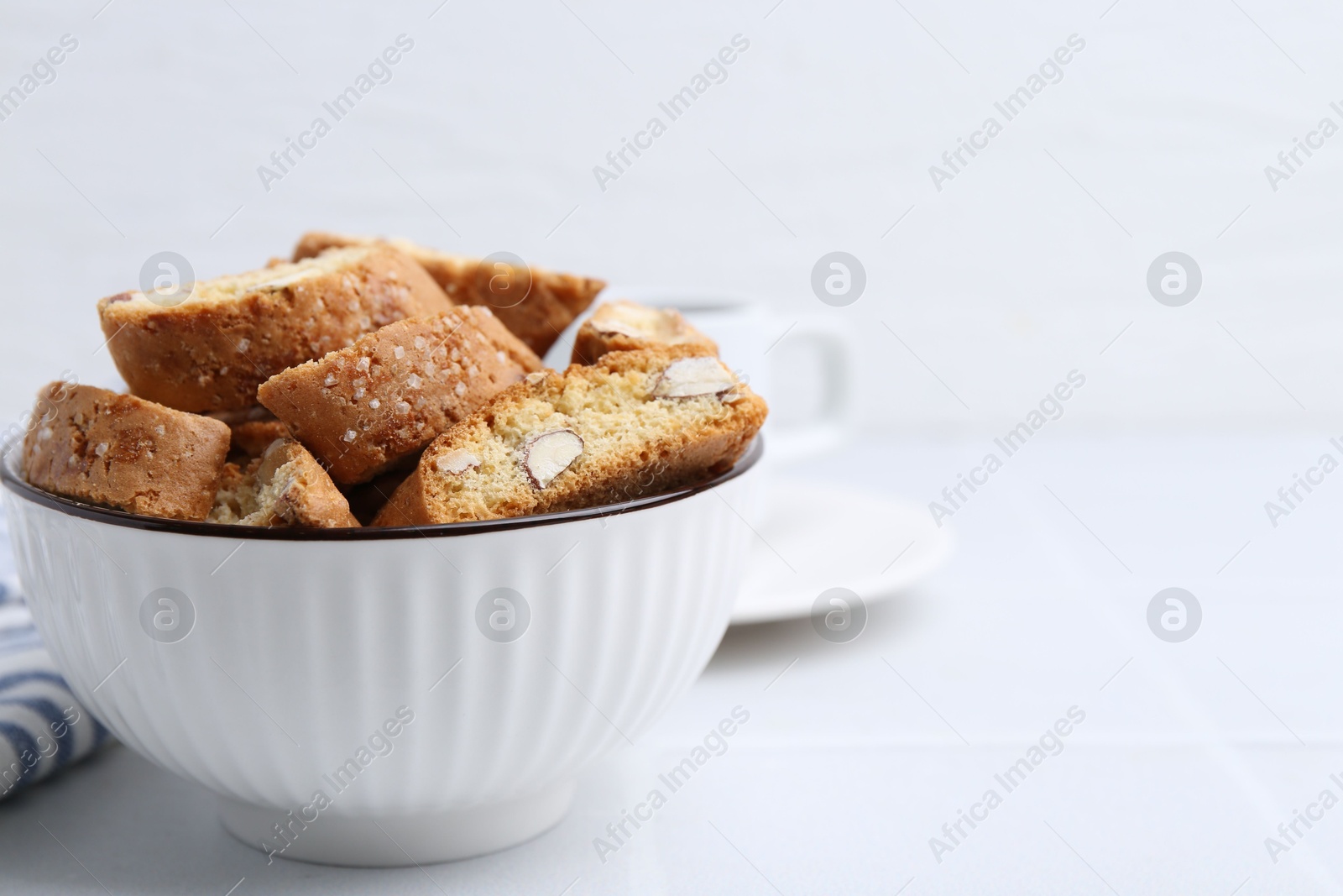 Photo of Traditional Italian almond biscuits (Cantucci) in bowl on white table, closeup. Space for text