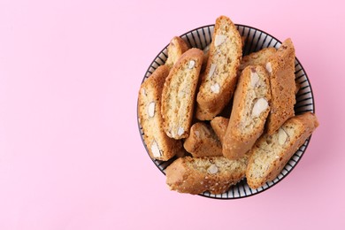 Photo of Traditional Italian almond biscuits (Cantucci) in bowl on pink background, top view. Space for text