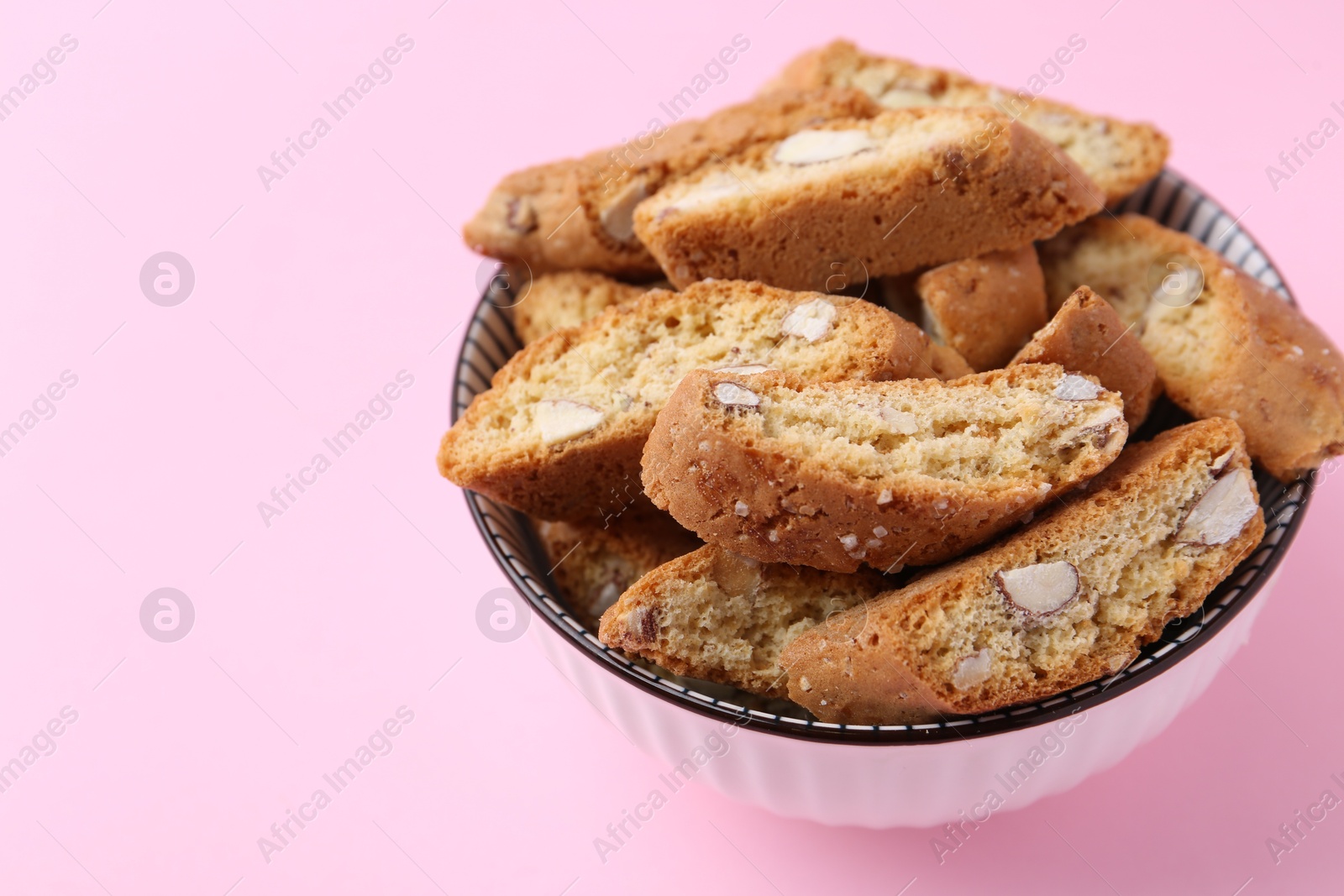 Photo of Traditional Italian almond biscuits (Cantucci) in bowl on pink background, closeup. Space for text