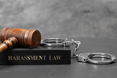 Harassment law book, judge's gavel and handcuffs on grey table, closeup