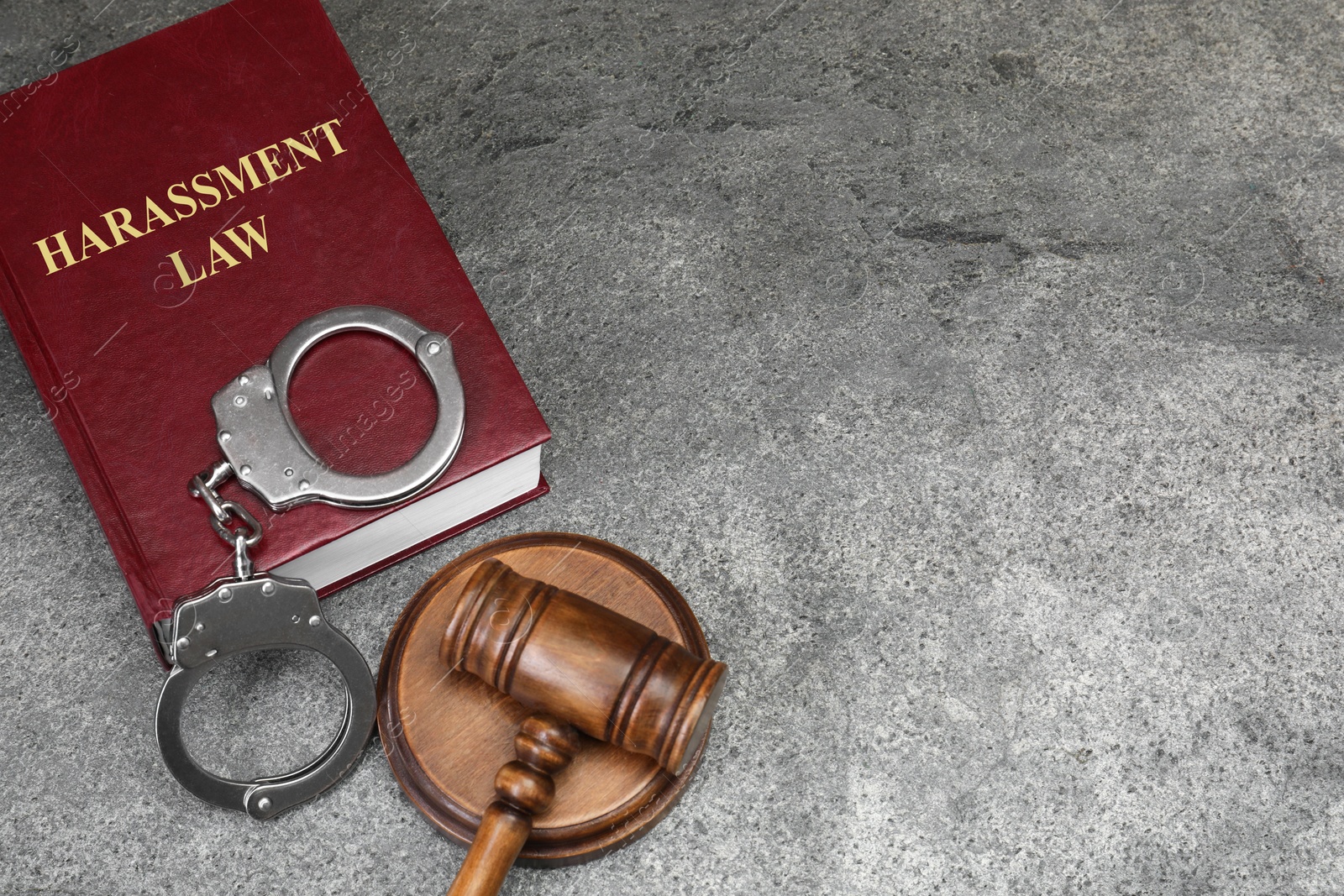 Image of Harassment law book, judge's gavel and handcuffs on grey table, above view