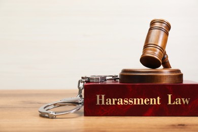 Image of Harassment law book, judge's gavel and handcuffs on wooden table, closeup