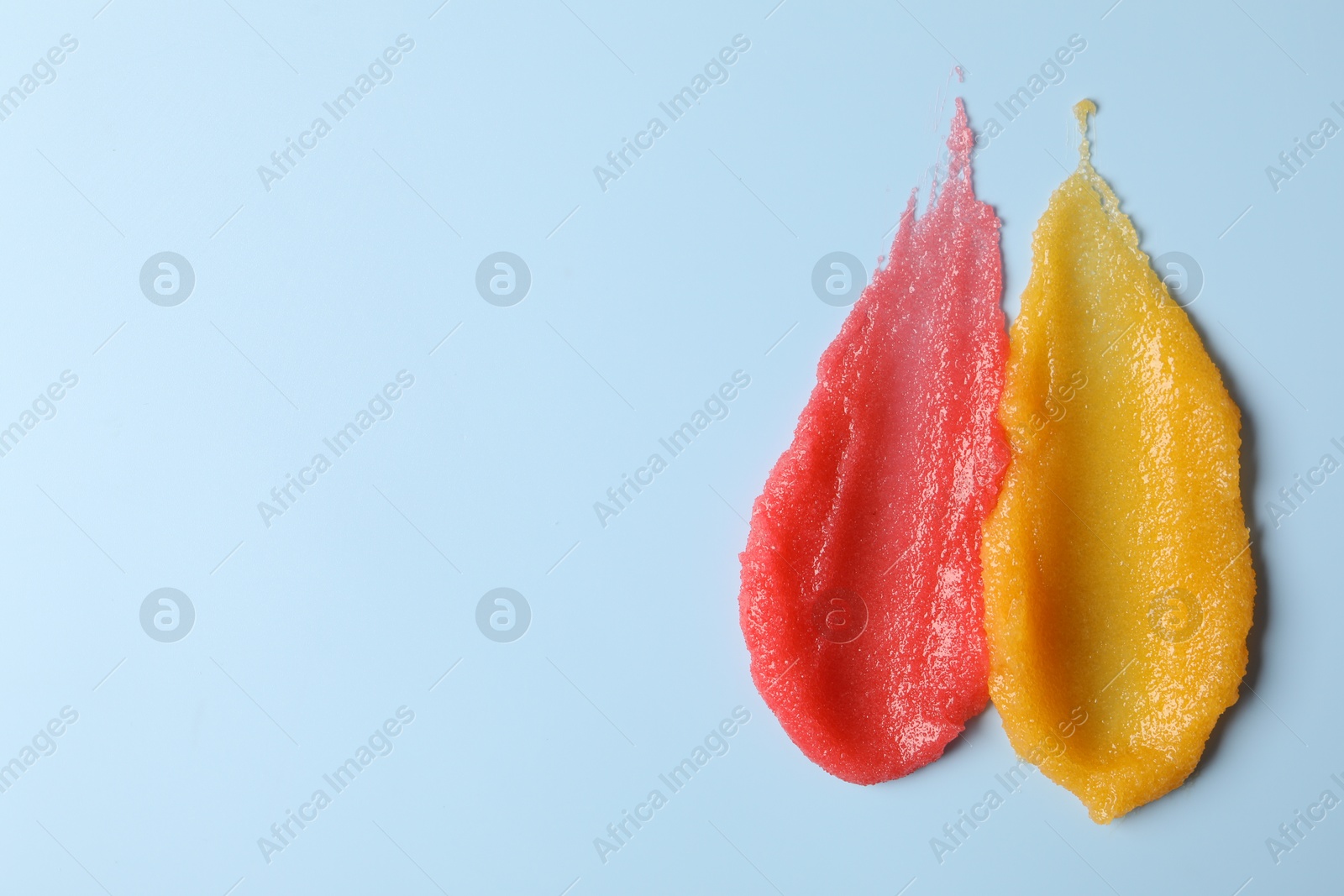 Photo of Smears of different body scrubs on light blue background, top view. Space for text