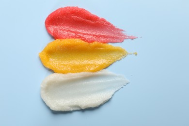 Photo of Smears of different body scrubs on light blue background, top view