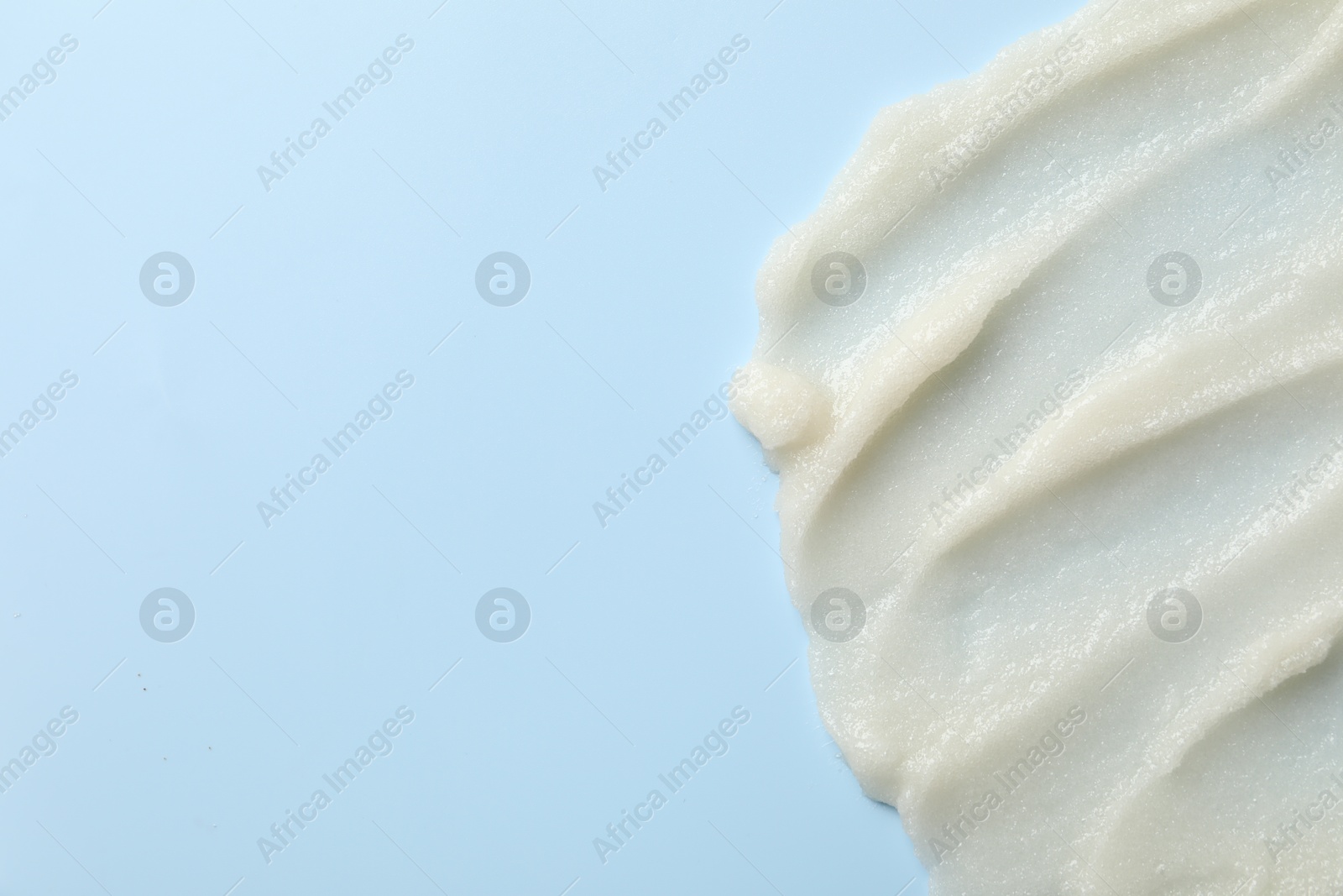 Photo of Smears of natural body scrub on light blue background, top view. Space for text