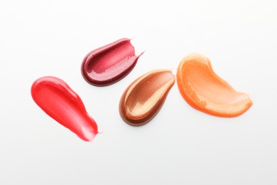 Photo of Smears of different lip products on white background, top view