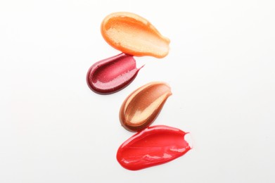 Photo of Smears of different lip products on white background, top view