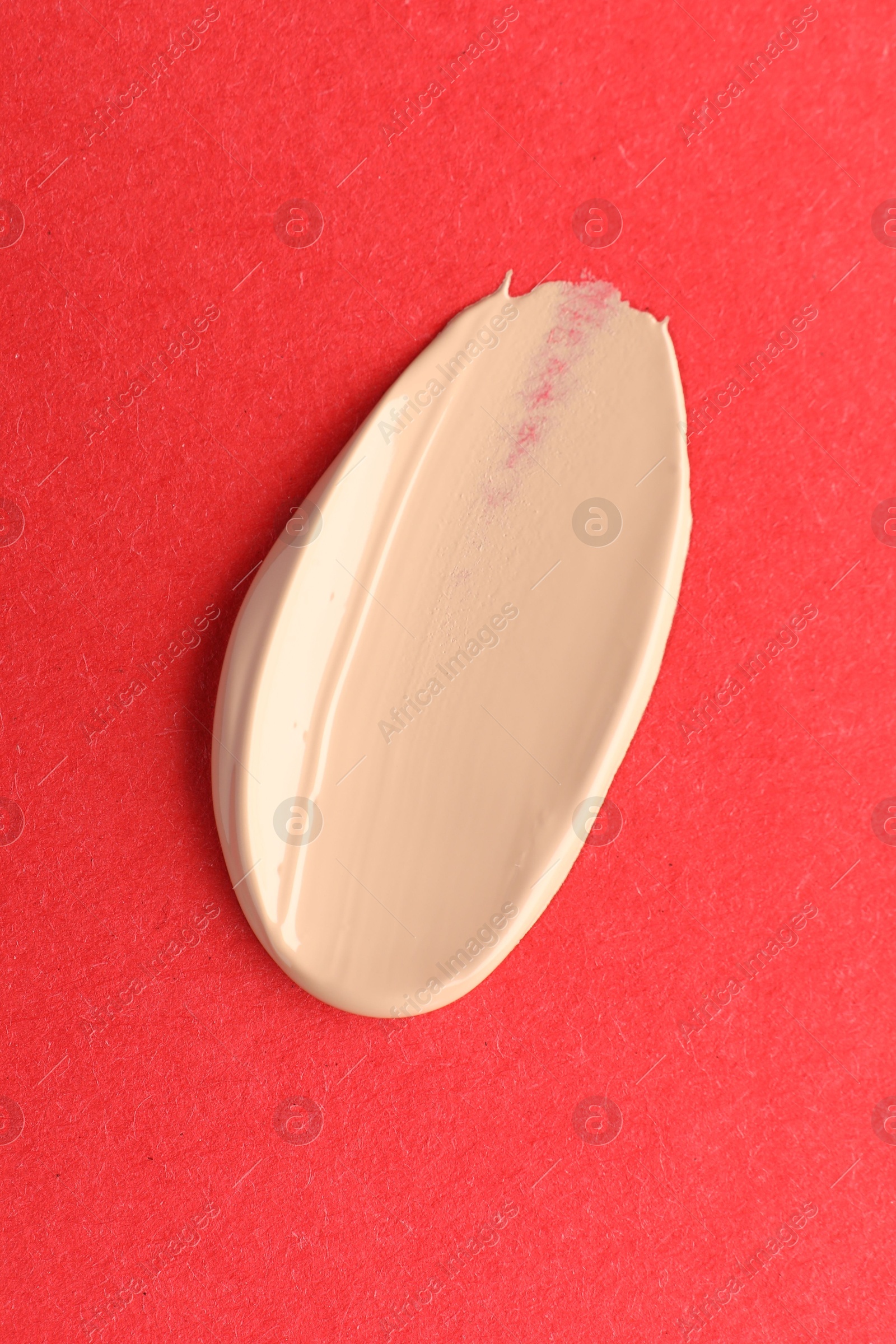 Photo of Smear of foundation on red background, top view