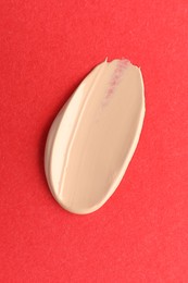 Photo of Smear of foundation on red background, top view