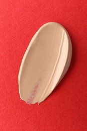 Photo of Smear of foundation on red background, top view