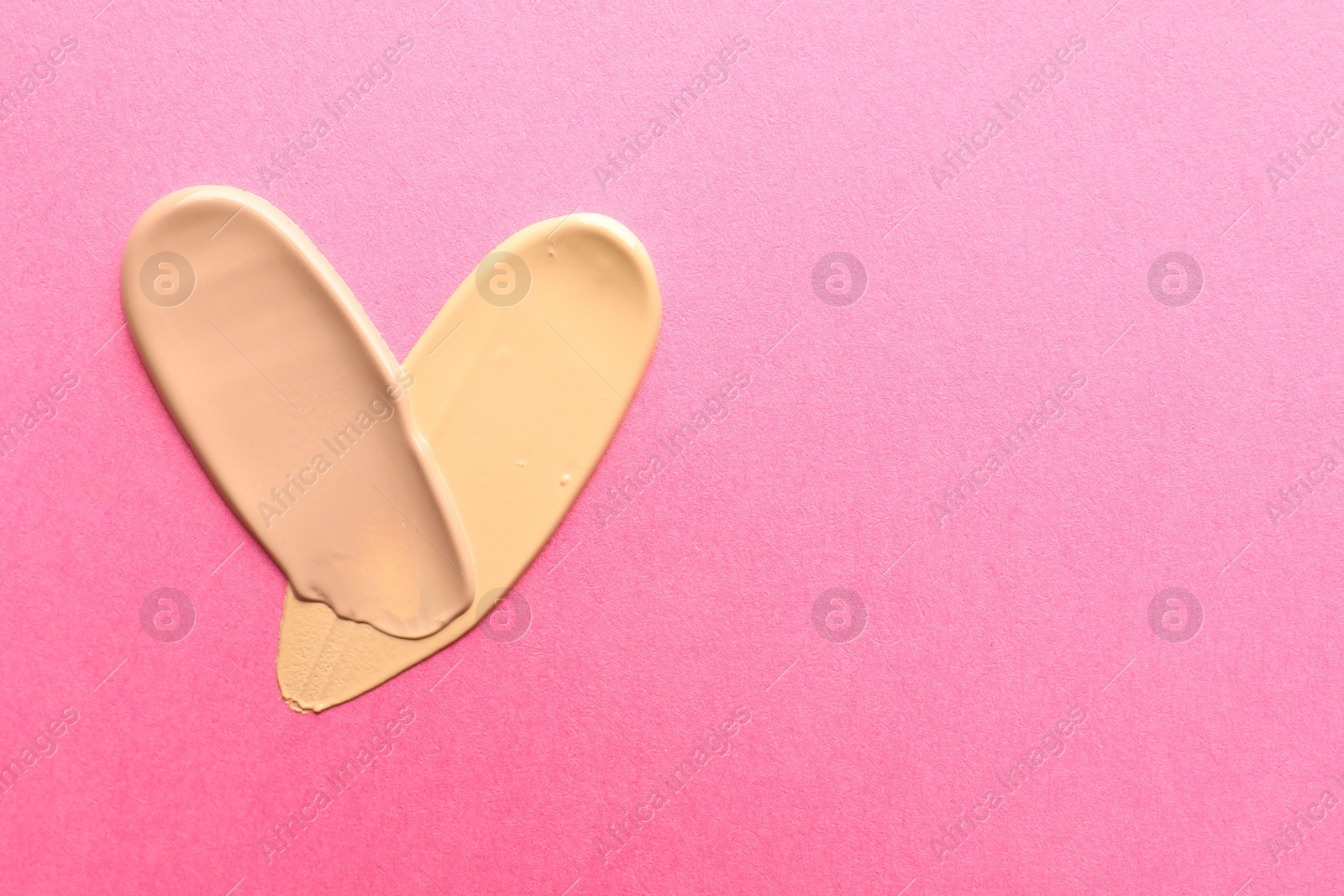 Photo of Foundation on pink background, top view with space for text. Smears of cosmetic product