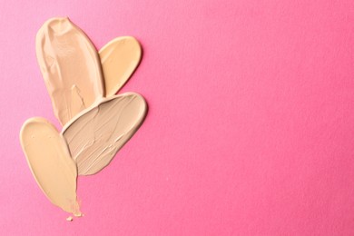 Photo of Foundation on pink background, top view with space for text. Smears of cosmetic product