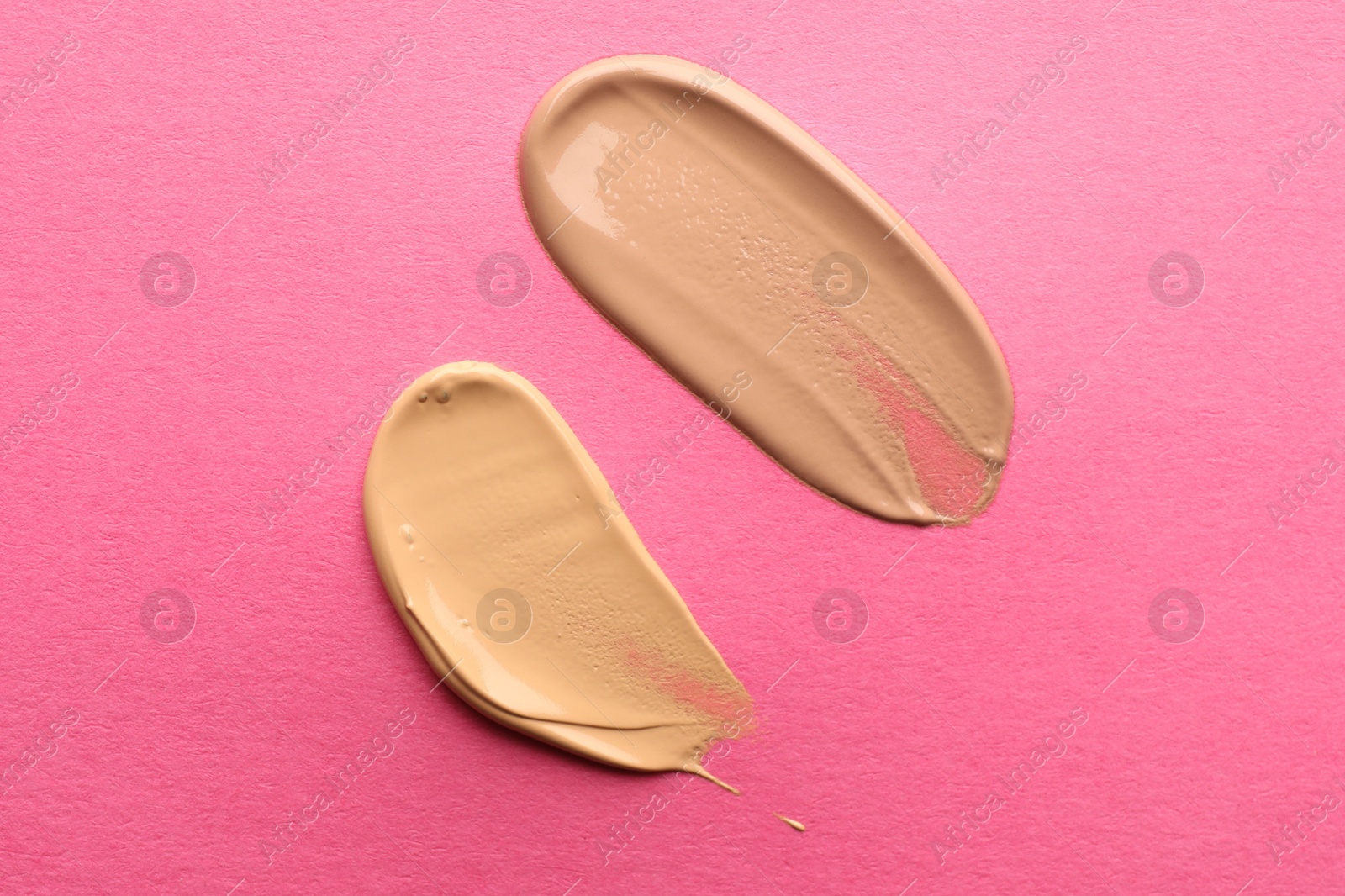 Photo of Foundation on pink background, top view. Smears of cosmetic product