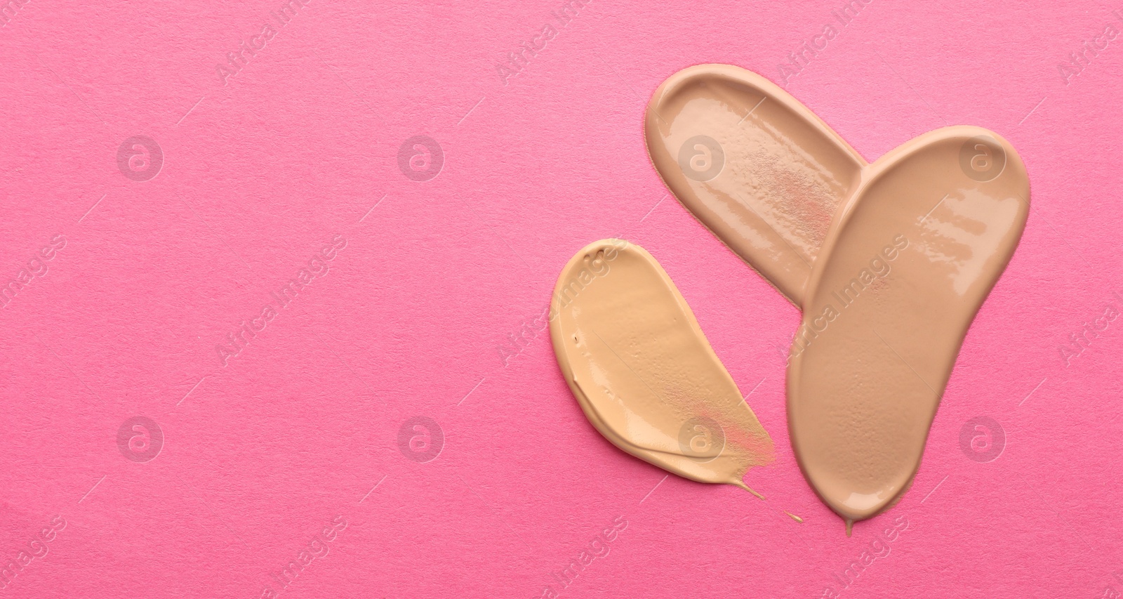 Photo of Foundation on pink background, top view with space for text. Smears of cosmetic product