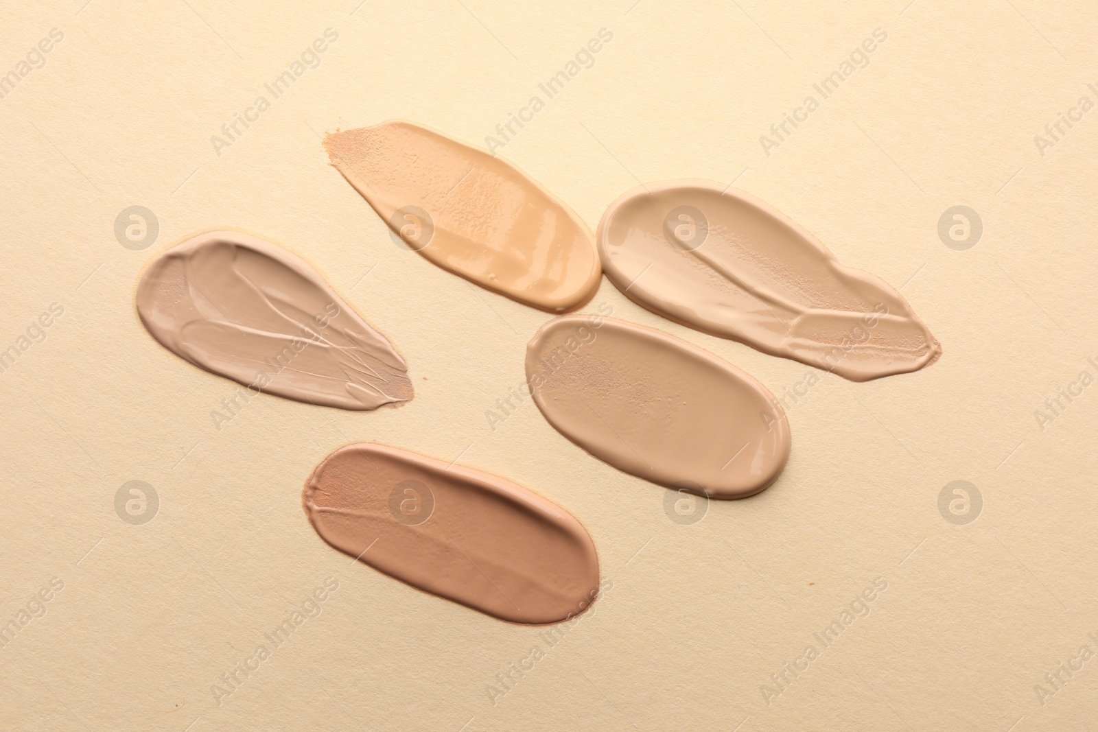 Photo of Samples of different foundations on beige background, closeup