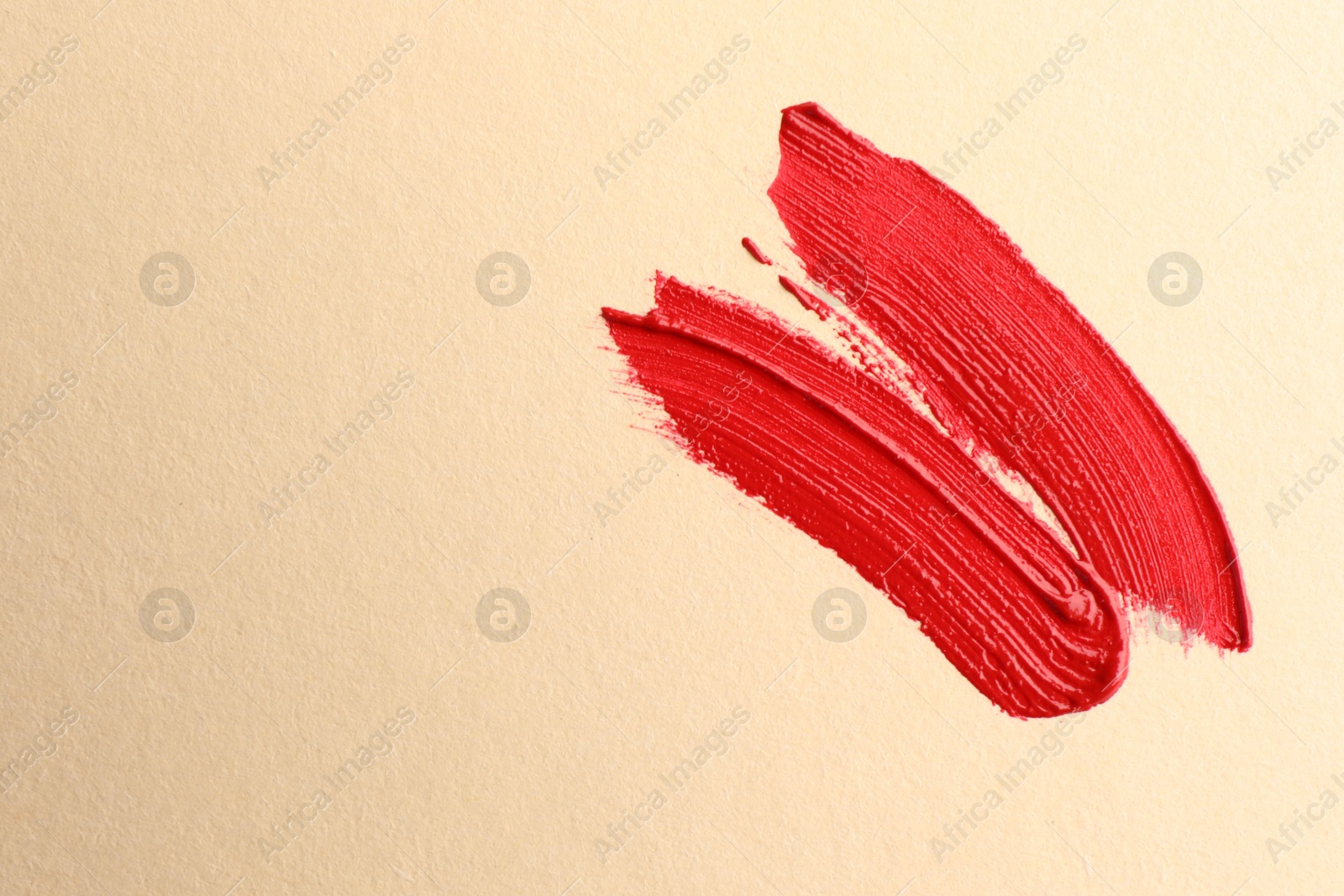 Photo of Red lipstick on beige background, top view with space for text. Smears of cosmetic product