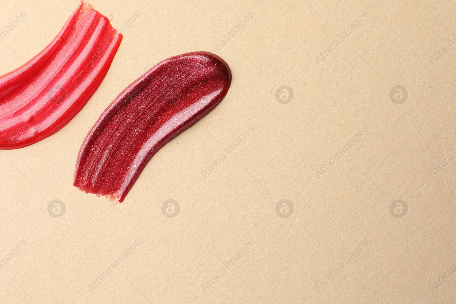 Photo of Lip glosses on beige background, top view with space for text. Smears of cosmetic products