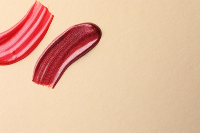 Photo of Lip glosses on beige background, top view with space for text. Smears of cosmetic products