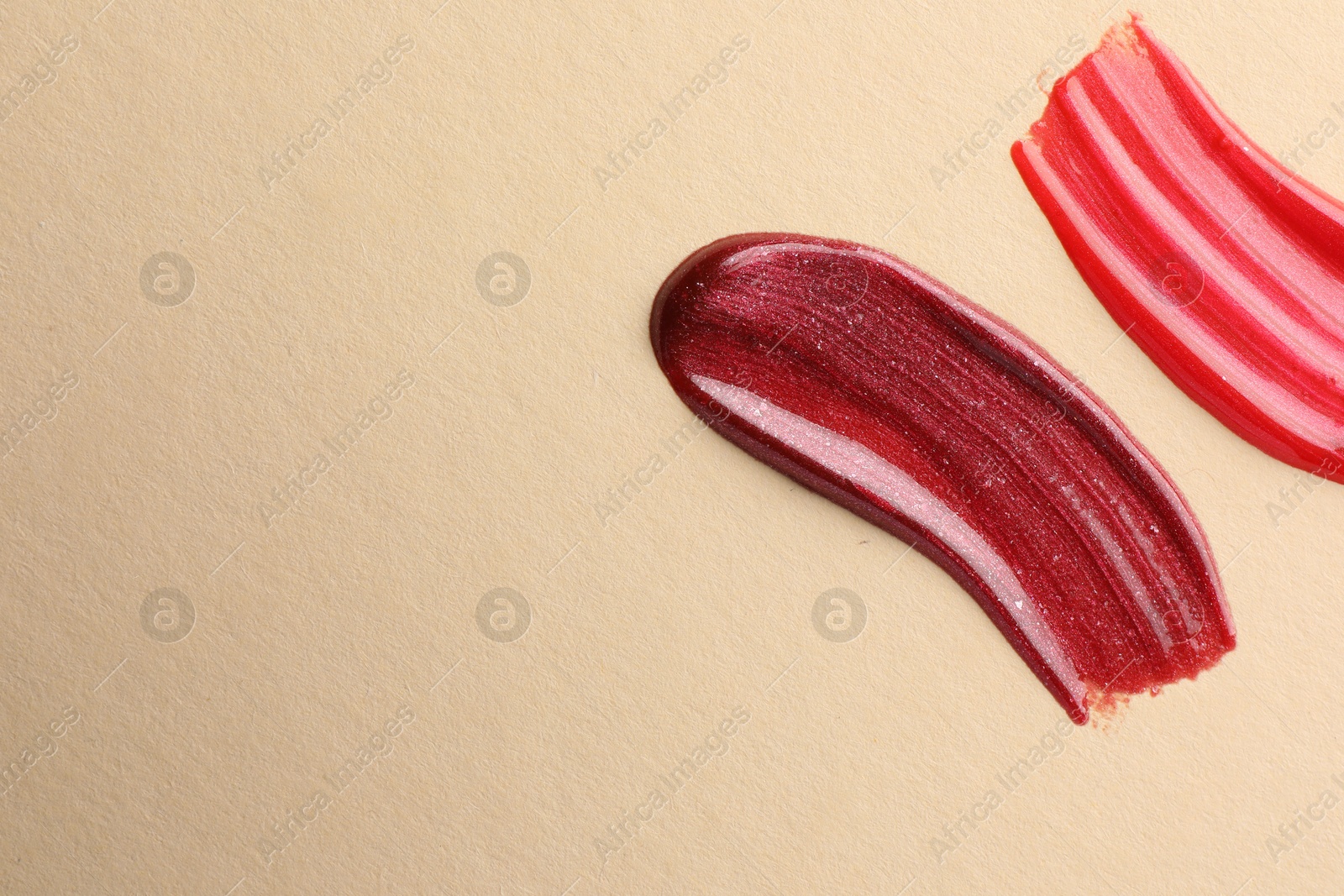 Photo of Lip glosses on beige background, top view with space for text. Smears of cosmetic products