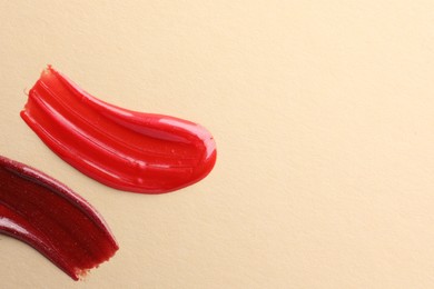 Photo of Lip glosses on beige background, top view with space for text. Smears of cosmetic products