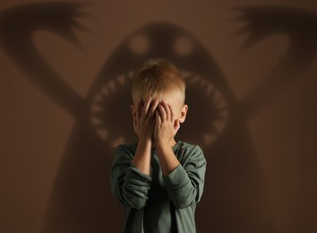 Illustration of Frightened by monsters, boy covering his eyes, teraphobia. Creepy shadows behind him