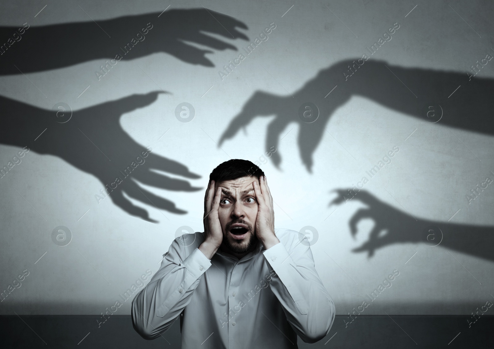 Image of Man scared by monstrous hands reaching for him. Creepy shadows on grey wall