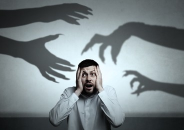 Image of Man scared by monstrous hands reaching for him. Creepy shadows on grey wall