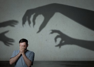 Image of Man scared by monstrous hands reaching for him. Creepy shadows on grey wall